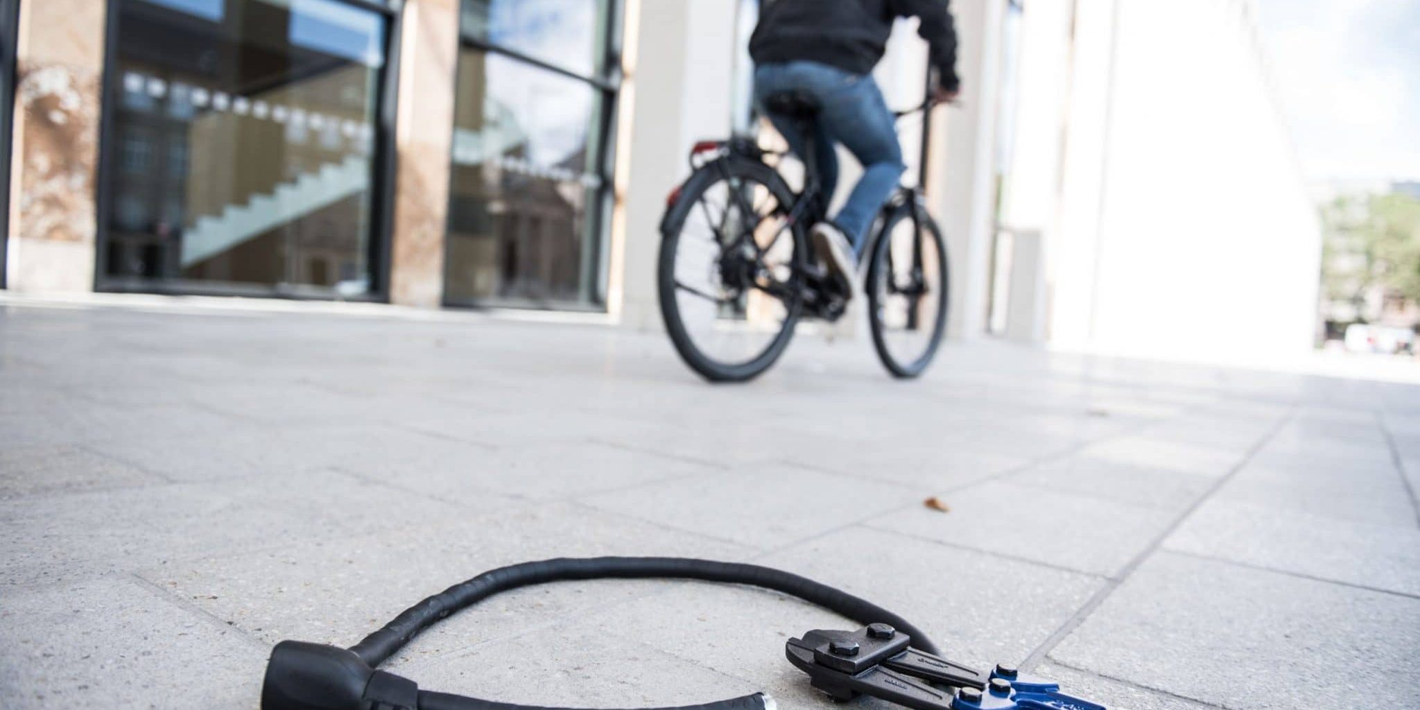 Mann fährt mit Fahrrad davon, aufgetrenntes Fahrradschloss liegt mit Zange auf dem Boden