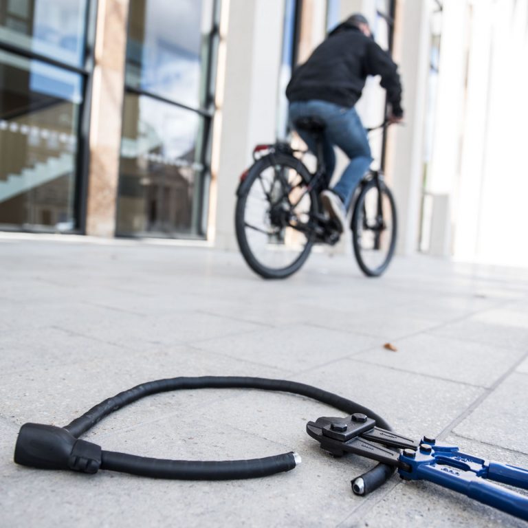Mann fährt mit Fahrrad davon, aufgetrenntes Fahrradschloss liegt mit Zange auf dem Boden